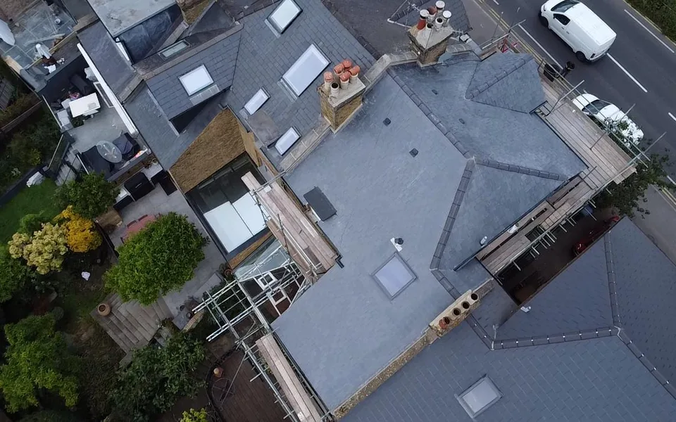 Drone view looking straight down on a large slate roof with rooflights on a corner house, scaffold along the street side