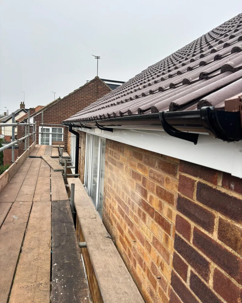 New brown tiles, white uPVC fascia and black guttering at the eaves, seen from the scaffold