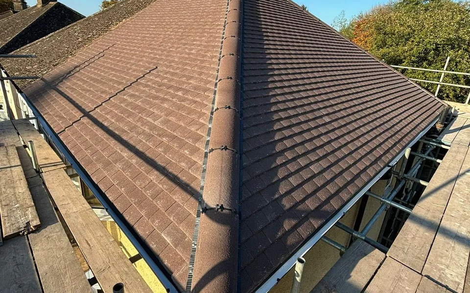 Hip of a brown concrete tile roof with black guttering along the eaves, seen from the scaffold