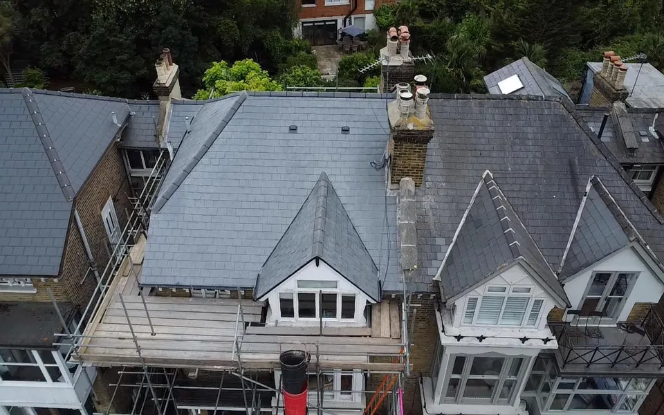 Drone view of slate roofs on a pair of period houses with gabled bays and brick chimney stacks, scaffold along the front