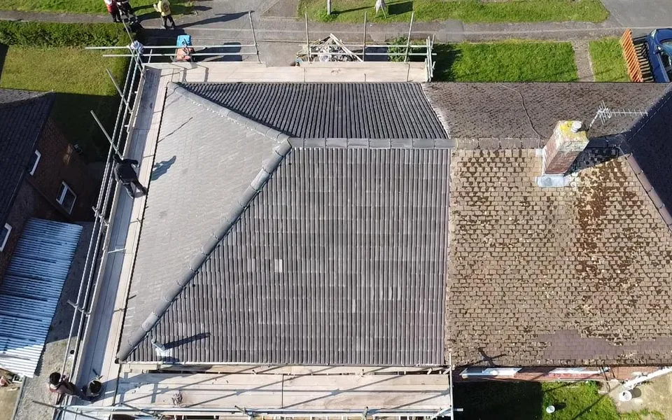 Drone view of a semi re-roofed in new grey concrete tile, beside the neighbour's original mossy roof