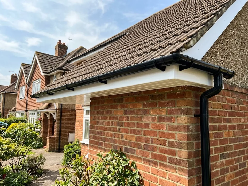 White uPVC fascia and soffit with black guttering and a black downpipe on a red brick house