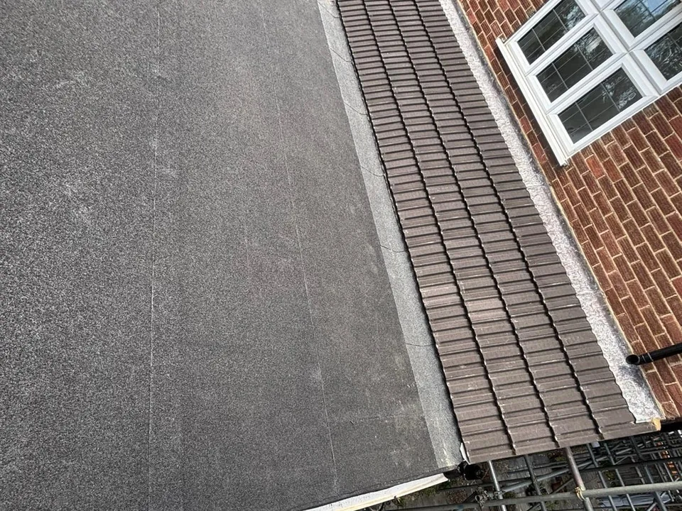 New flat roof with a mineral finish meeting a tiled slope beside a brick wall
