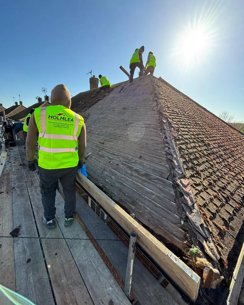The Holmlea Roofing team in hi-vis working on the ridge of a re-roof in the sunshine