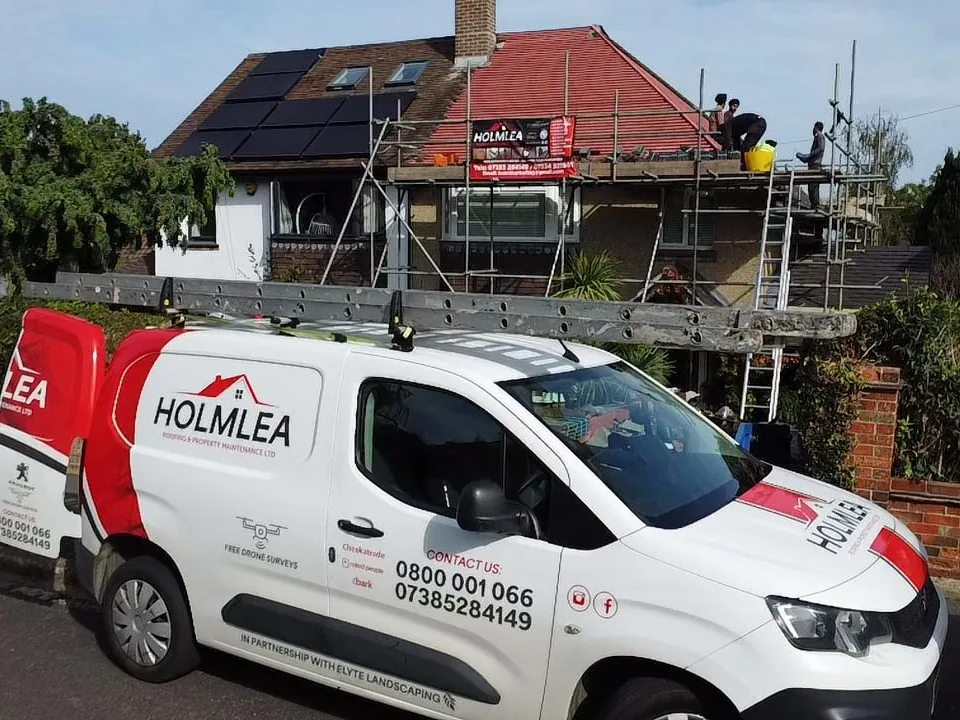 The Holmlea Roofing van outside a scaffolded house, with the Holmlea banner on the scaffold and the team at work on the roof